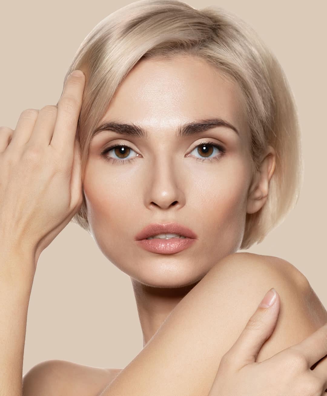 Beautiful woman with short blonde hair holds her hand to her face and models facial treatments.