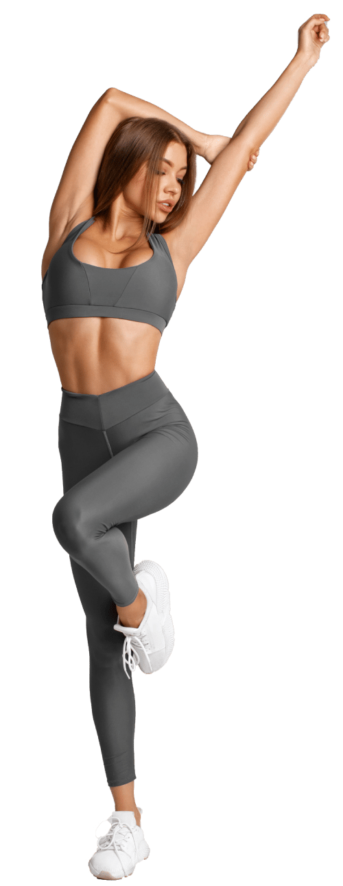 Fit, toned woman in grey workout clothes stands on one leg with her arms in the air.
